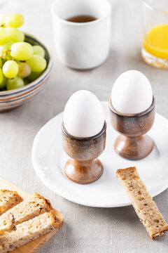 Two white eggs in ceramic egg cups with breakfast setting