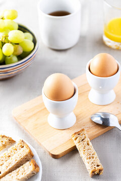 Two brown eggs in white egg cups on wooden board for breakfast