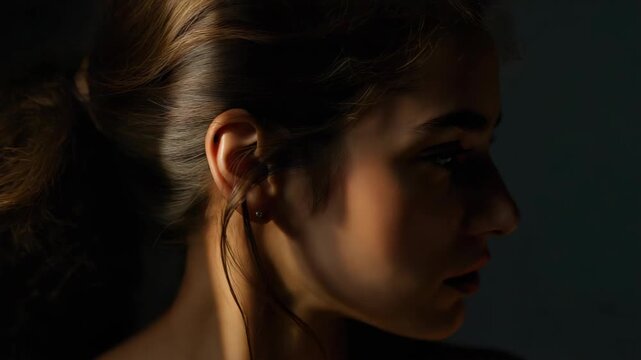 Young woman portrait with dramatic side lighting, shadowed warm window light and contemplative