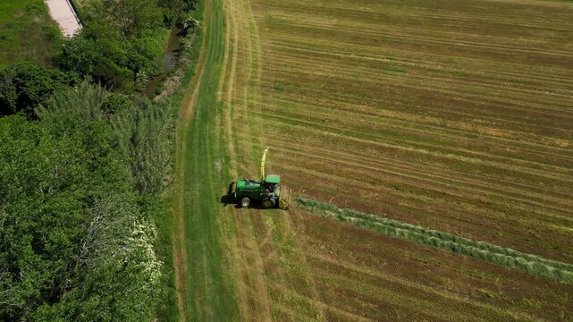 An agricultural tractor mows a field, creating a swathe of freshly cut hay, symbolizing the hard work and dedication of farming.