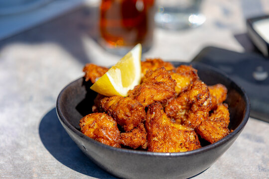 Kibbeling is a Dutch snack consisting of battered chunks of fish in black bowl with a piece of lemon, Commonly served with a mayonnaise-based garlic sauce or tartar sauce, Holland's favorite snacks.