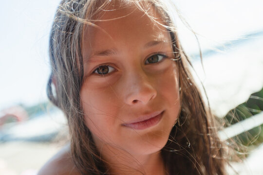 Beautiful girl with dark hair blowing in the wind looks at camera on bright sunny summer day at the beach. Child captures natural portrait of childhood innocence. Kid in carefree peaceful mood