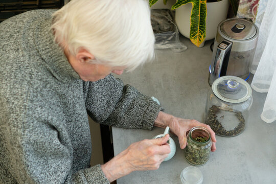 Top view of an elderly man spooning tea leaves into a teapot. The image captures quiet moment of daily routine and self-care. Senior citizen preparing hot beverage.