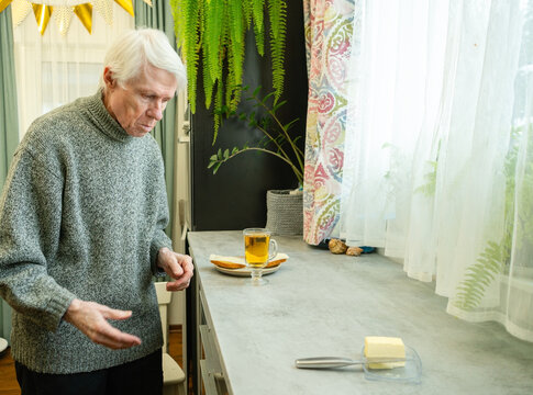 A senior citizen stands before kitchen counter where tea and butter sandwiches are laid out. The image captures moment of readiness before meal of senior. Elderly man self-catering.