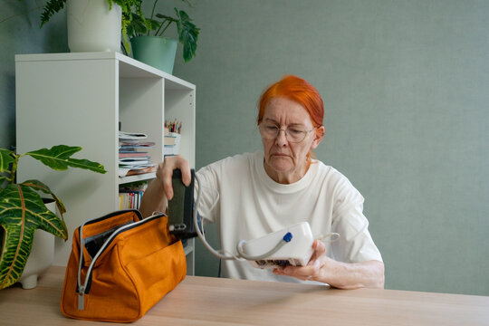A senior woman organizes her blood pressure monitor and its accessories neatly on the table, preparing for a health check.