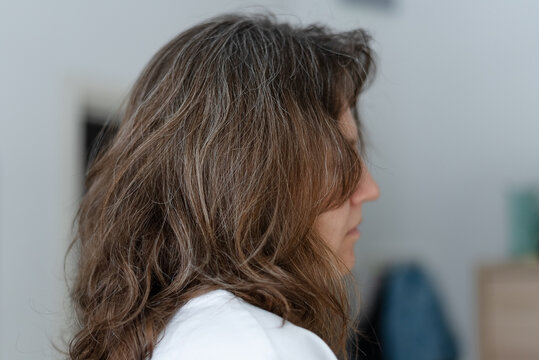 A woman prepares to dye her graying hair going through coloring procedure. The mature adult applies chemical treatment to cover silver strands temporarily. Mother hides natural aging signs.