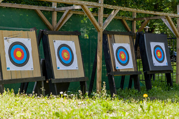 Colourful archery targets on wooden stands in a grassy range with green netting, daisies, wildflowers, and trees in sunny weather, Tallinn, Estonia