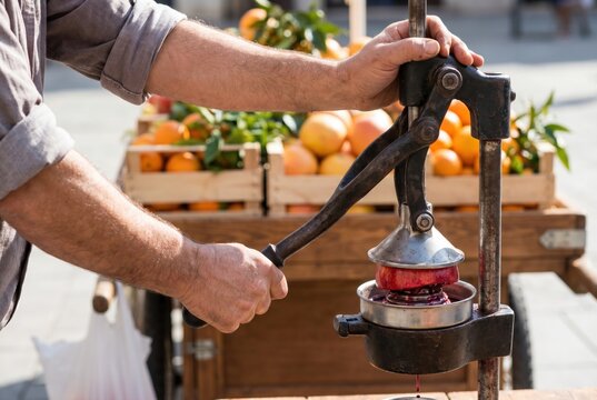 Street vendor hands operating a heavy vintage cast iron manual citrus juicer to squeeze a red pomegranate