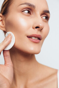 A woman gently wipes her cheek with a cotton pad during a skincare routine, showcasing a radiant complexion, calm focus, and a self care moment in soft lighting.