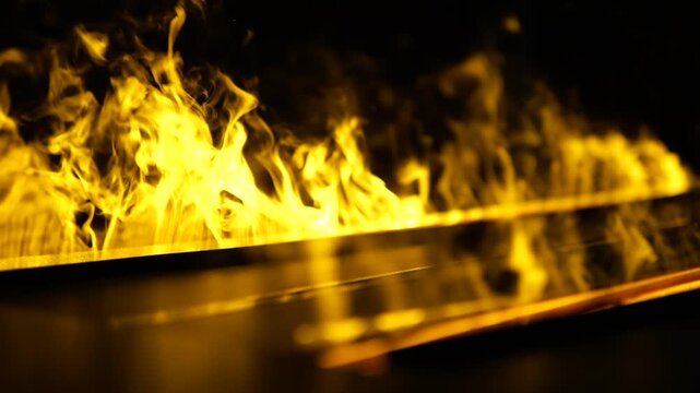 Intense golden flames burning brightly and producing smoke in slow motion against a dark black background, creating an abstract and powerful visual of fire, heat, and combustion energy