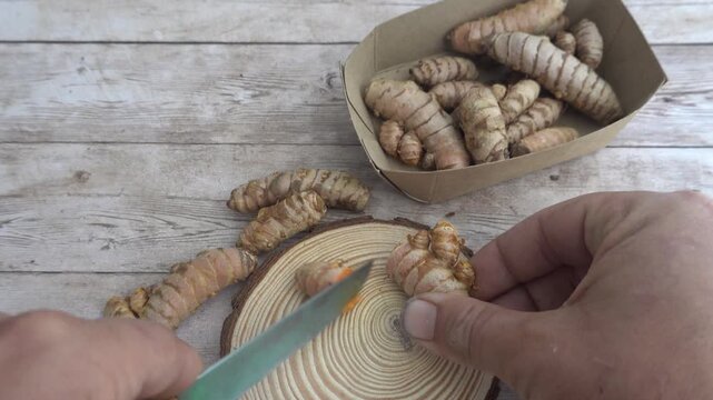 Male hands slicing fresh turmeric root with a knife on a wooden background