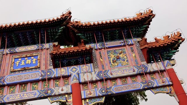 Richly decorated imperial archway with painted beams in Summer Palace. View of layered rooflines, carved panels, Chinese characters and vivid blue gold colors under cloudy sky, Beijing, China, 4k