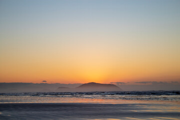 Fototapeta premium Golden Sunrise Over Ocean with Mountain Silhouette