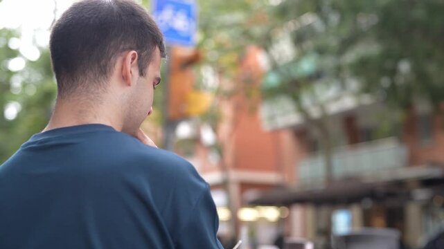 Man walks past street, smoking cigarette. He pauses, glances around. He continues walking, thoughtful. Urban backdrop, trees, buildings blur softly. Ideal for lifestyle, travel, or urban scenes