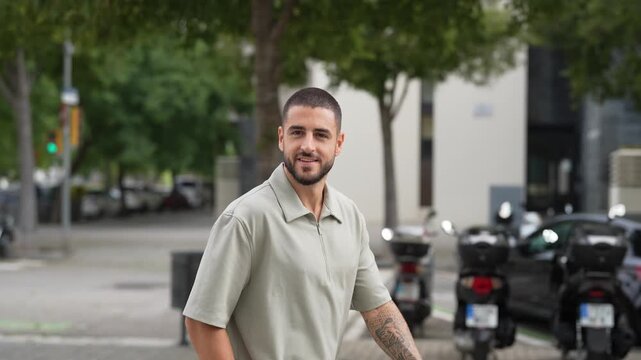 Man walks city street, pauses to look at camera. He smiles warmly, showing friendly expression. Urban setting with trees, cars, and bikes. Ideal for lifestyle or business travel themes