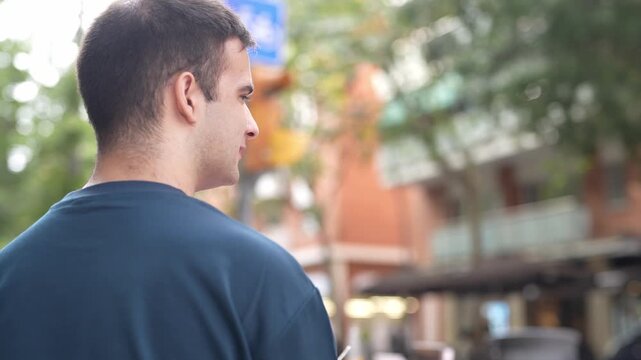 Man walks city street, thoughtful, unaware. Trees and buildings blur softly behind him. His gaze follows direction, not looking back. Urban life feels distant, personal, calm