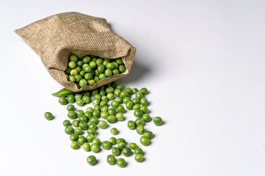 Green peas spilling from burlap sack on white