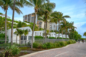 Fototapeta premium White architectural bungalows and palm trees in Miami. Modern white round roof buildings behind metal fence with palm trees on beach walk in Miami Florida.