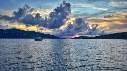 Sailboats anchored at sunset beneath dramatic clouds in a calm Caribbean bay, with warm horizon light and tranquil ocean textures creating a peaceful, cinematic travel scene. © Scott
