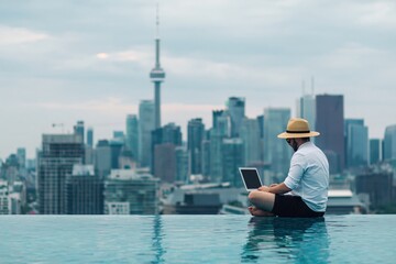 Naklejka premium Man in a straw hat using a laptop by an infinity pool, overlooking the Toronto city skyline with the CN Tower