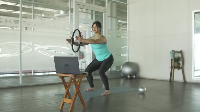 Woman doing online pilates class with magic circle