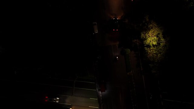 Top down aerial night shot of vehicles crossing an intersection over a main highway with headlights glowing.