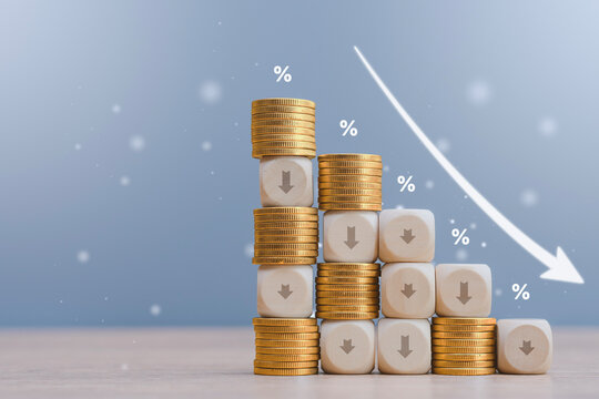 Wooden blocks with down arrows and golden coins arranged in a declining graph pattern against a blue background. Concept for mortgage rate reduction, deflation and financial crisis.