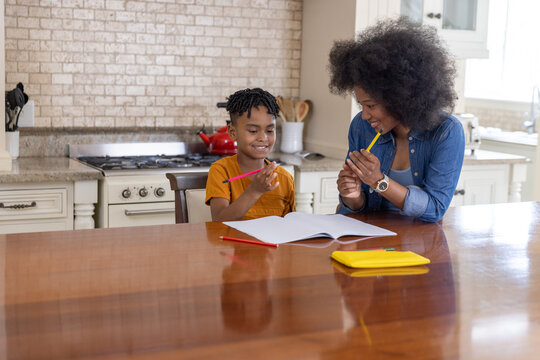 African American mother and son leaning over notebook at kitchen table using colored pencils