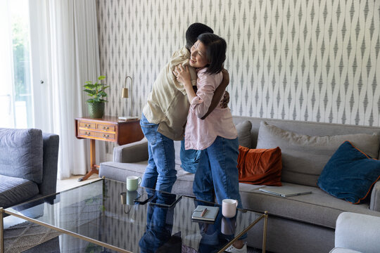 Asian woman and African American man embracing in living room by glass-top coffee table with mugs