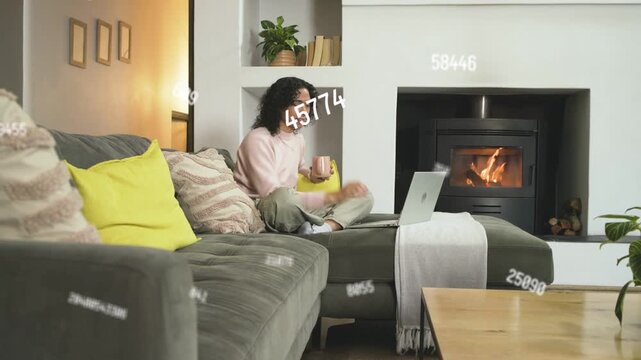 Tech worker sipping mug and tapping laptop in home den showing numeric overlays for analyzing data