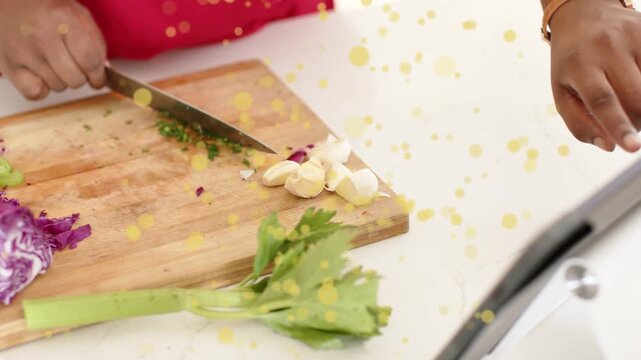 Woman chopping herbs, dicing veggies on board, checking tablet for cooking, yellow dots overlaying