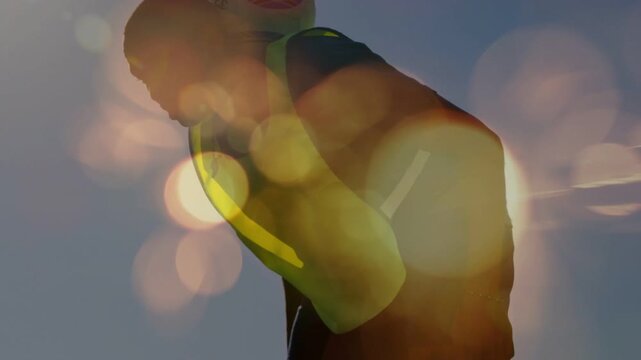 Man leaning forward against sky after exertion for safety, warm bokeh drifting across yellow vest