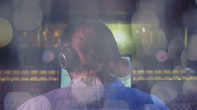 Male audio pro sitting at console, hearing DAW cue and adjusting headphones with bokeh around head