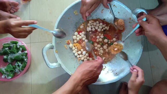 Group of people eating spicy Indonesian Seblak together from a traditional metal wok, communal dining lifestyle concept.