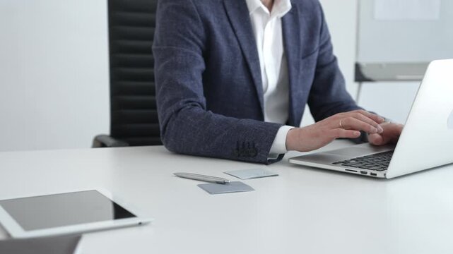 Professional businessman in glasses working on a laptop, analyzing financial data and charts in a modern, bright office setting, focusing on business growth and strategy