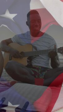 Vertical video: Guitarist starting song by sea, friend passing cup, flag overlay drifting, bonding