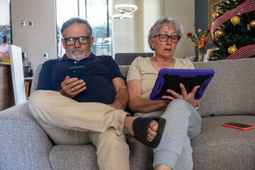 Obraz premium Senior couple using digital devices on sofa at home
