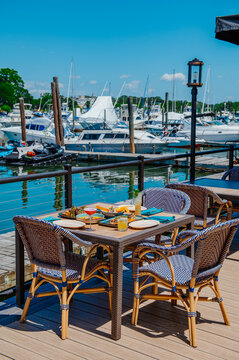 Outdoor dining table with seafood and cocktails at marina. Full table setting with fish, meat, appetizers and drinks at waterfront restaurant with luxury yachts.