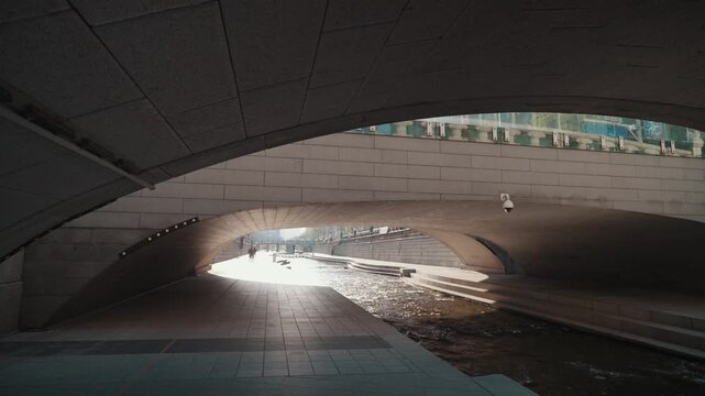 Moody view of Cheonggyecheon Stream under urban bridges with soft light reflections on water surface. Calm and cinematic atmosphere in Seoul city.