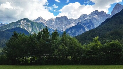 Majestic Alpine Mountain Range with Dense Green Forest and White Clouds  © AndriHernawan
