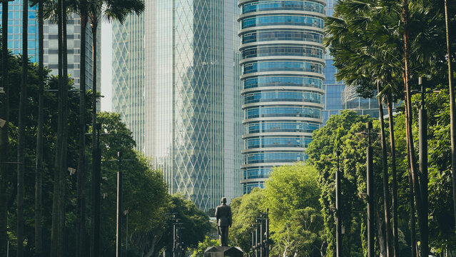 Long shot of skyscrapers and the Ir. Soekarno or Sukarno statue at Gelora Bung Karno (GBK) Sports Complex is surrounded by trees.