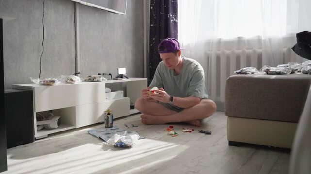 White Man Assembling Model Kit On Floor In Sunlit Apartment Living Room, Timelapse Captures Stepbystep Construction With Scattered Pieces And Focused Hands, Purple Cap And Casual Clothes, Media