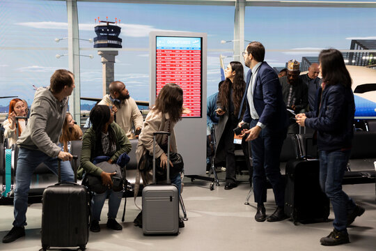 Worried about disruption, delayed flight and passengers in airport reacting to red alert on airline screen. Receiving bad news, flight cancellation and international travelers expressing anxiety