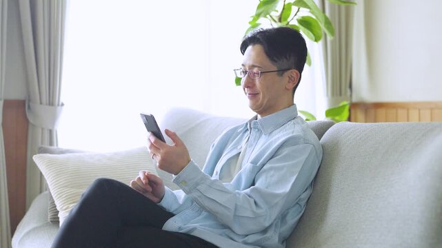 ソファでスマートフォンを使う男性のライフスタイルイメージ, Man Using Smartphone on Sofa at Home