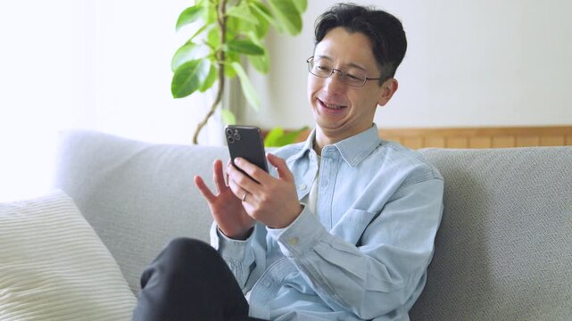ソファでスマートフォンを使う男性のライフスタイルイメージ, Man Using Smartphone on Sofa at Home