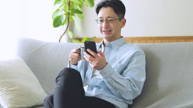 コーヒーを飲みながらスマートフォンを使う男性のライフスタイルイメージ, Man Using Smartphone While Drinking Coffee at Home