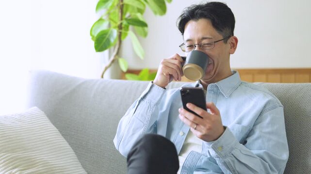 コーヒーを飲みながらスマートフォンを使う男性のライフスタイルイメージ, Man Using Smartphone While Drinking Coffee at Home