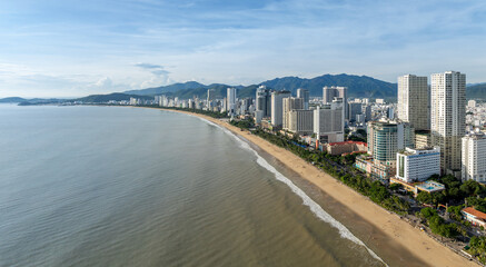 Obraz premium Aerial view of Nha Trang beach, Vietnam. The city's coastline is lined with hotels and palm trees, with mountains in the background.