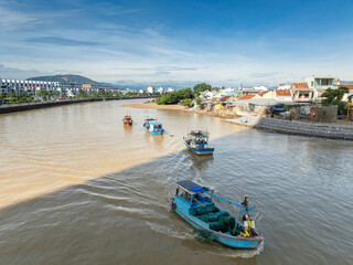 Fototapeta premium Fishing boats navigate the Cai River in Hoi An, Vietnam, carrying nets and supplies. The scene captures daily life and commerce in this historic port city.