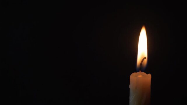 Single burning candle flame glowing in the dark background